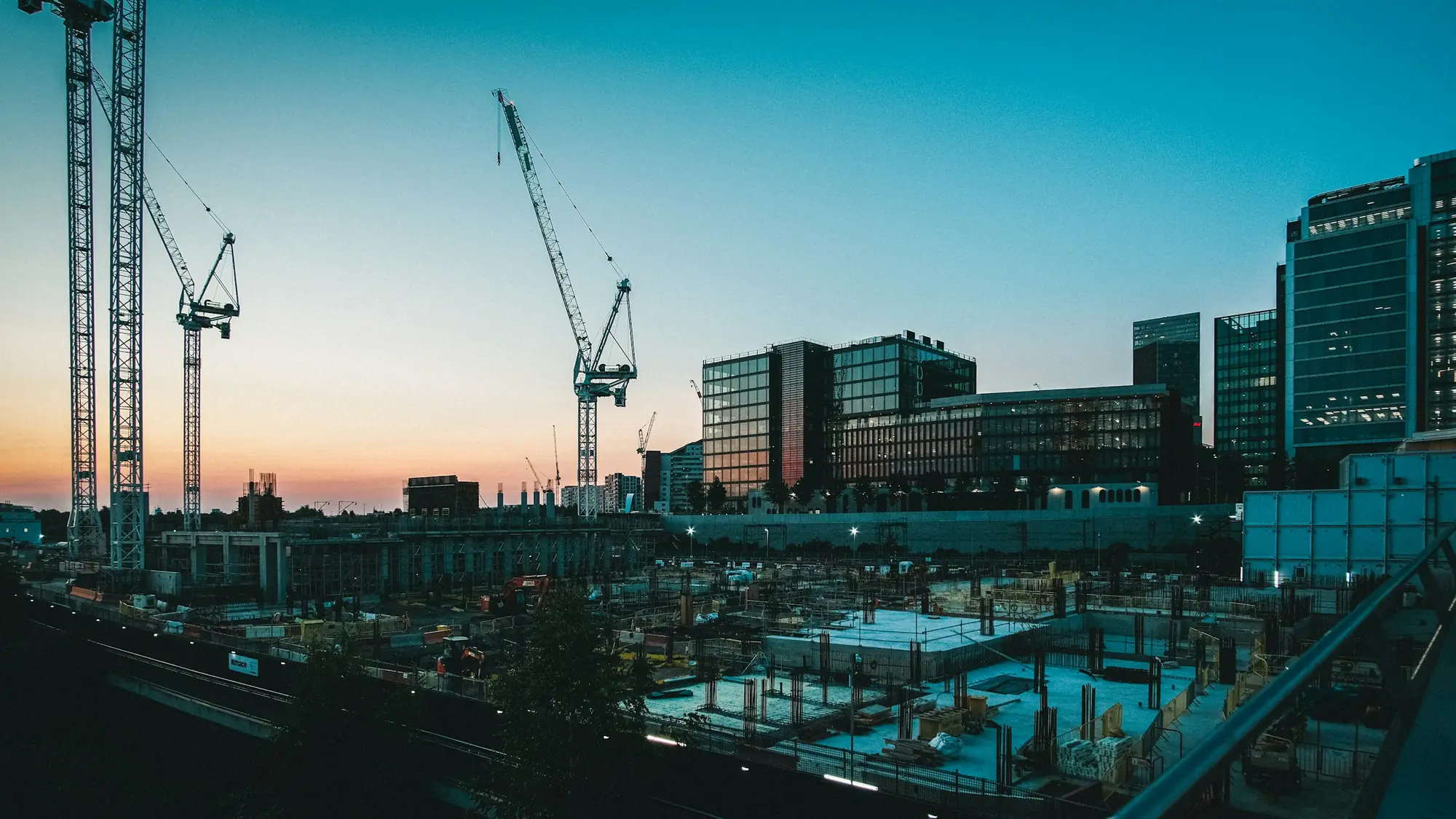 Große Baustelle mit Kränen und Neubauten in der Abenddämmerung